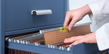 Person holt sich eine Akte mit der Ziffer zweiundzwanzig aus dem Aktenschrank heraus.