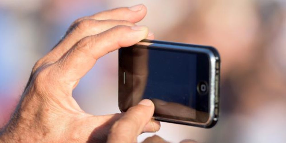 Mann hält sein Smartphone in der Hand und fotografiert etwas.