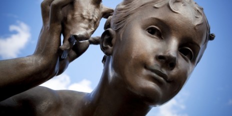 Statur mit einem kleinen Jungen der eine Muschel an Ohr hält.