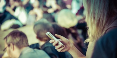 In einer Menschenmengen hält eine Frau ihr Smartphone in der Hand.