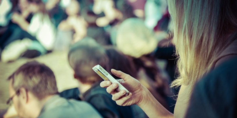 In einer Menschenmengen hält eine Frau ihr Smartphone in der Hand.