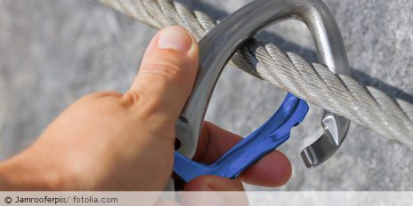 Hand hängt Karabiner in ein Stahlsein ein.