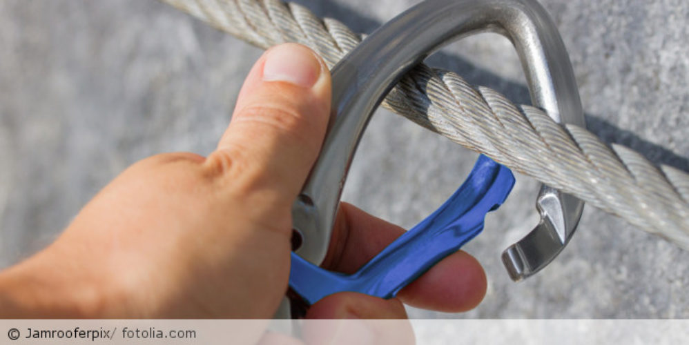 Hand hängt Karabiner in ein Stahlsein ein.
