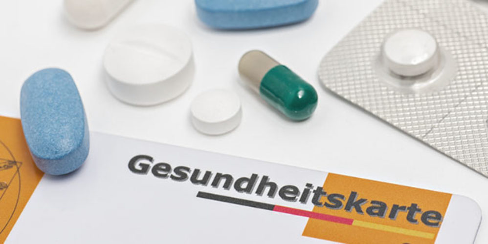 Verschiedenfarbende Tabletten die auf einer Gesundheitskarte drauf liegen.