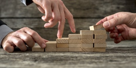Mehrere Hände die mit Klötzen eine kleine Treppe bauen.