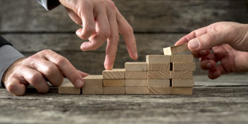 Mehrere Hände die mit Klötzen eine kleine Treppe bauen.