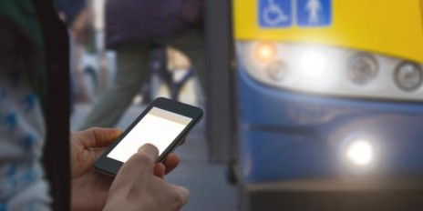 Eine Person tippt auf seinem Smartphone und wartet auf den Bus.