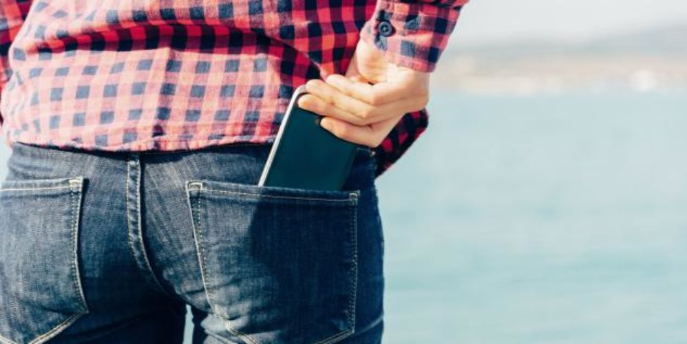 Mann steckt sein Smartphone in seien hintere Hosentasche.
