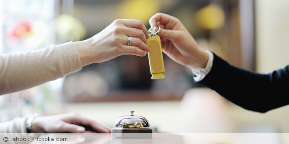 Person checkt an Hotelrezeption ein und bekommt Schlüssel übergeben.