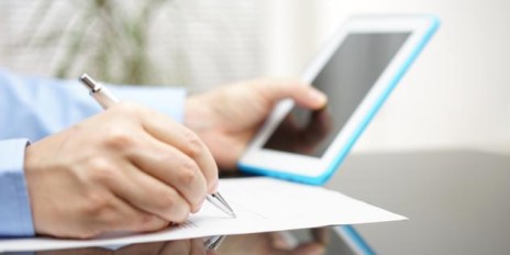 Person hält sein IPad in der Hand und unterschreibt etwas auf einem Blattpapier.