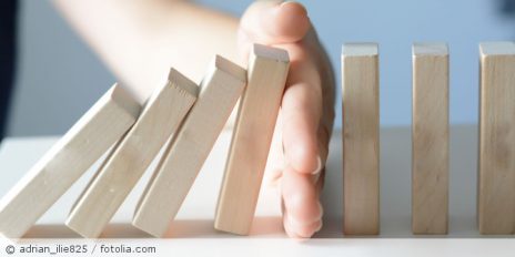 Eine Person die aufgestellte Domino-Steine stoppt.