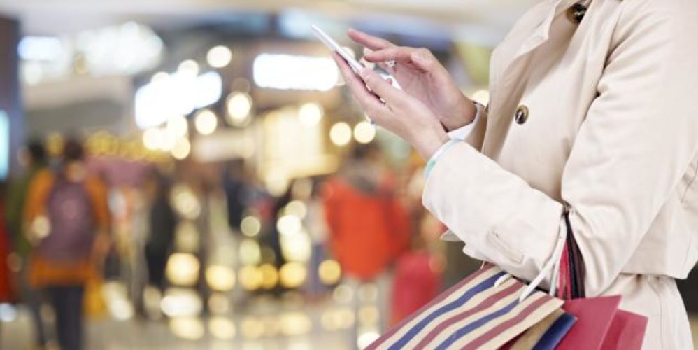 Eine Frau in einen Shopping-Center mit einen Handy in der Hand.