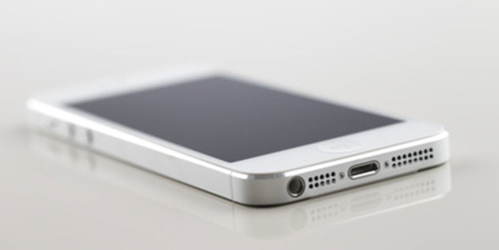 Weißer Smartphone liegt auf einem Weißen Glastisch.
