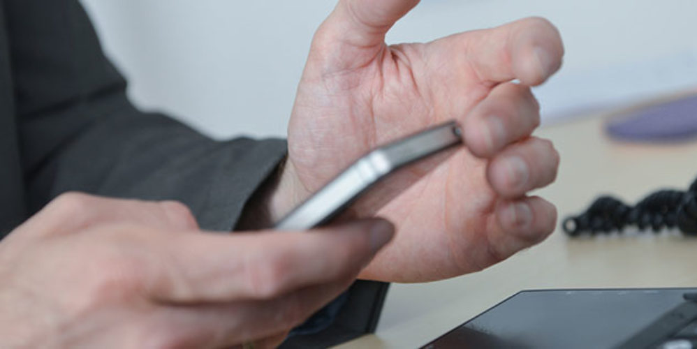 Mann hält sein Smartphone mit den beiden Händen und tippt was drauf.