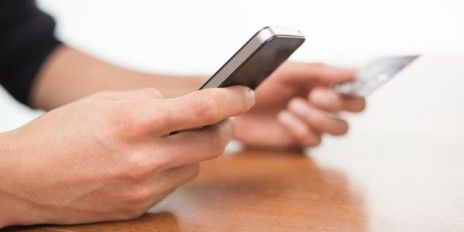 Person hält in einer Hand sein Smartphone und in der anderen Hand seine Kreditkarte.