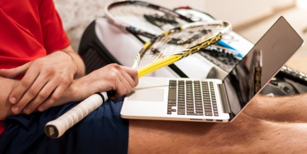Eine Person mit einen Schläger in der Hand und davor ein Laptop.