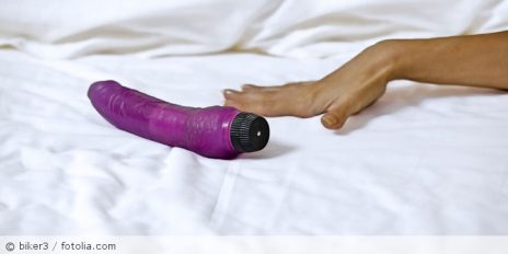 Eine Hand, neben der ein Vibrator auf einen Bett ist.
