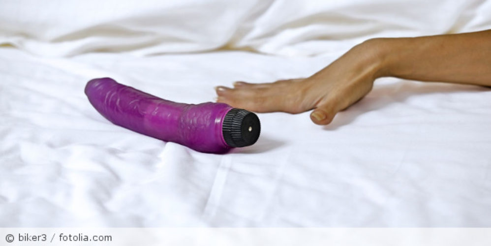 Eine Hand, neben der ein Vibrator auf einen Bett ist.