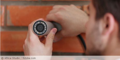 Ein Mann der eine Videokamera an der Hauswand installiert.