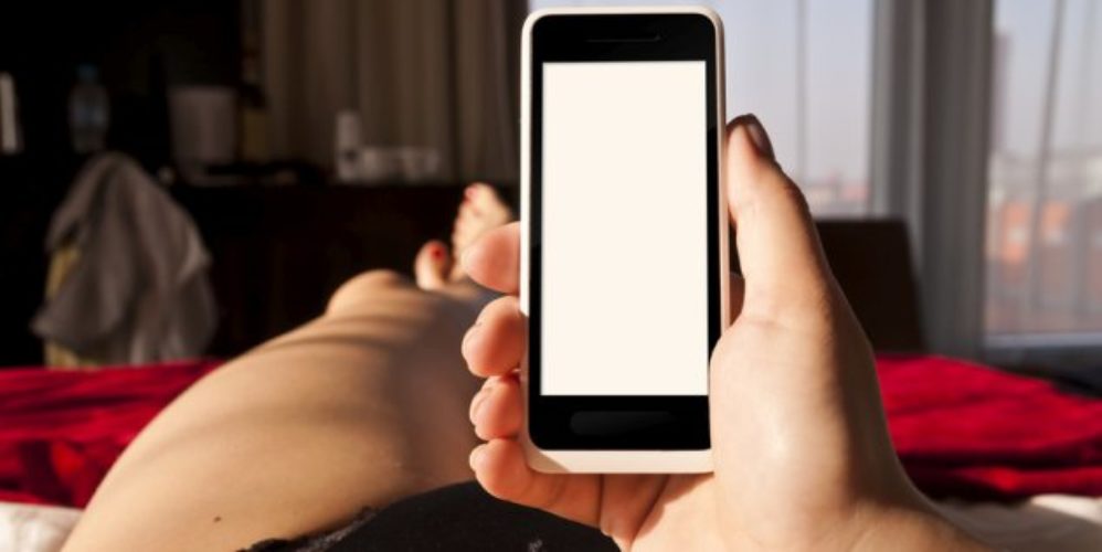 Frau liegt auf dem Bett und hält ihr Smartphone in der Hand.