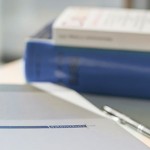 Ein Block mit einem Kugelschreiber liegen auf einem Tisch, im Hintergrund liegen Bücher über den BDSG.