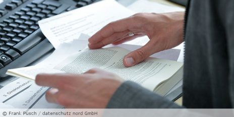Ein Mann blättert in einem Praxishandbuch, im Hintergrund liegt eine schwarze Tastatur.