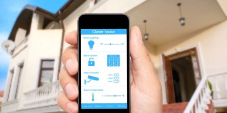 Mann hält sei Smartphone vor seinem Haus.