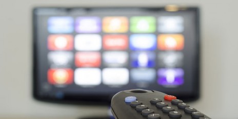 Im Vordergrund eine Fernbedienung und im Hintergrund ein Fernseher.