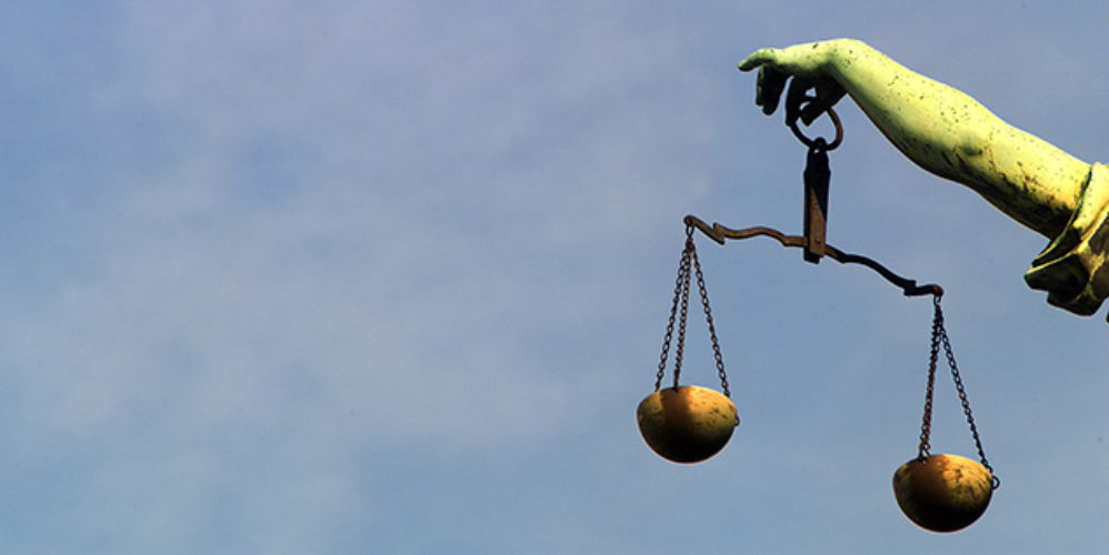 Justitia wo man nur ihr Arm und die Waage auf dem Bild sieht.