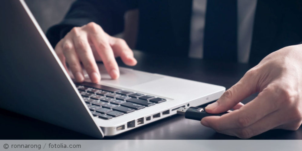 Mann steckt USB-Stick in einen Laptop.
