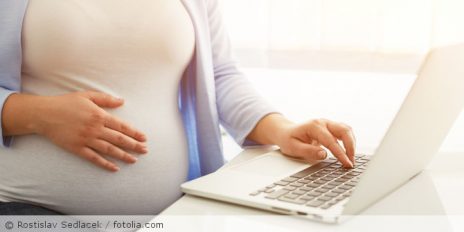 Eine schwangere Frau an einen Laptop.