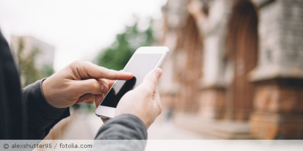 Eine Person mit einen Handy in der Hand vor einer Kirche.