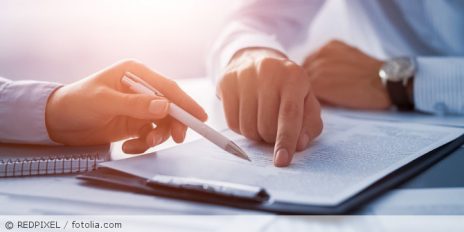 Zwei Personen halten ihre Finger auf ein Dokument.
