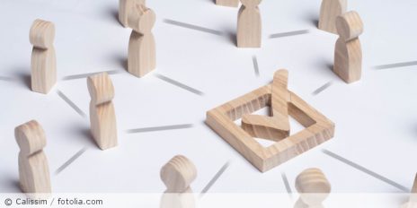 Menschen als Holzfiguren und in der Mitte ein Quadrat mit einen Pfeil in der Mitte.