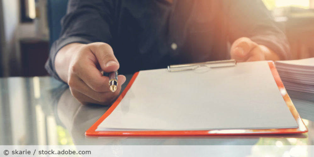Person mit Dokument und Stift in der Hand.
