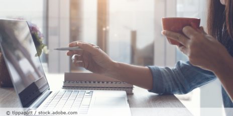 Frau zeigt etwas auf ihrem Laptop und hält eine Tasse in der Hand.
