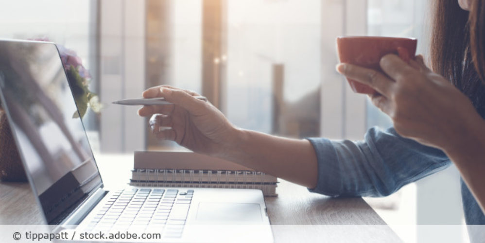 Frau zeigt etwas auf ihrem Laptop und hält eine Tasse in der Hand.
