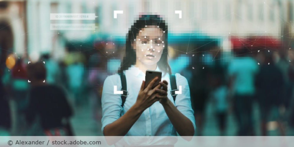 Frau läuft durch Innenstadt mit Handy in der Hand. Um ihr Gesicht ist eine Gesichtserkennung.