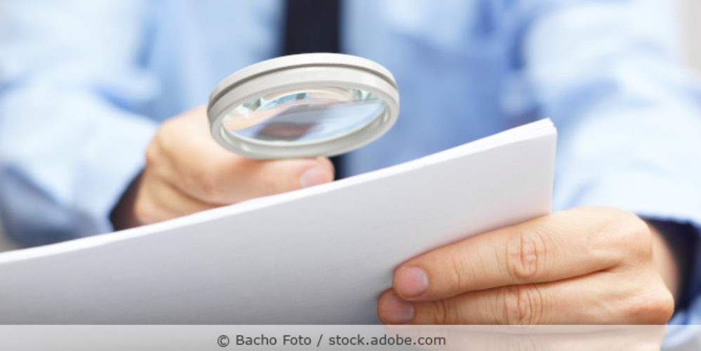 Geschäfstmann untersucht Papier mit einer Lupe