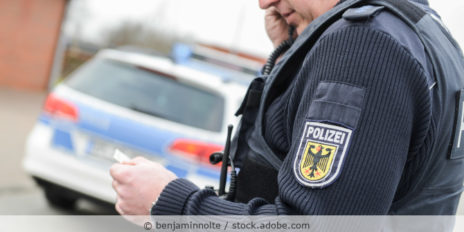 Polizist steht vor seinem Wagen und telefoniert