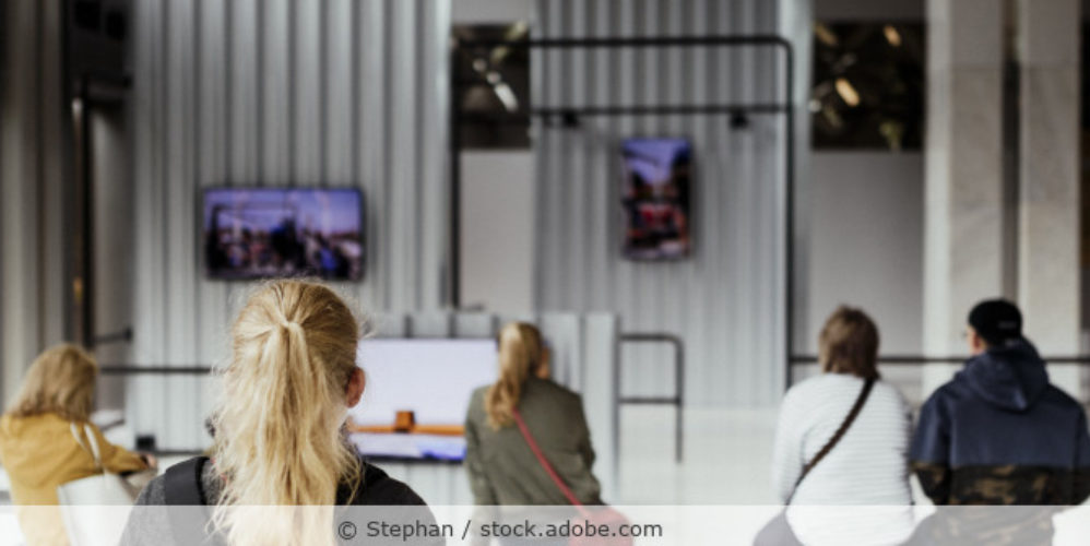 Menschen sitzen im Museum und schauen auf Monitore
