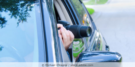 Ein Detektiv mit Kamera sitzt im Auto und fotografiert durch das geöffnete Autofenster.