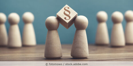 Holzspielfiguren auf einem Tisch und zwischen zwei Figuren ist ein Holzwürfel mit dem Paragraph-Symbol.