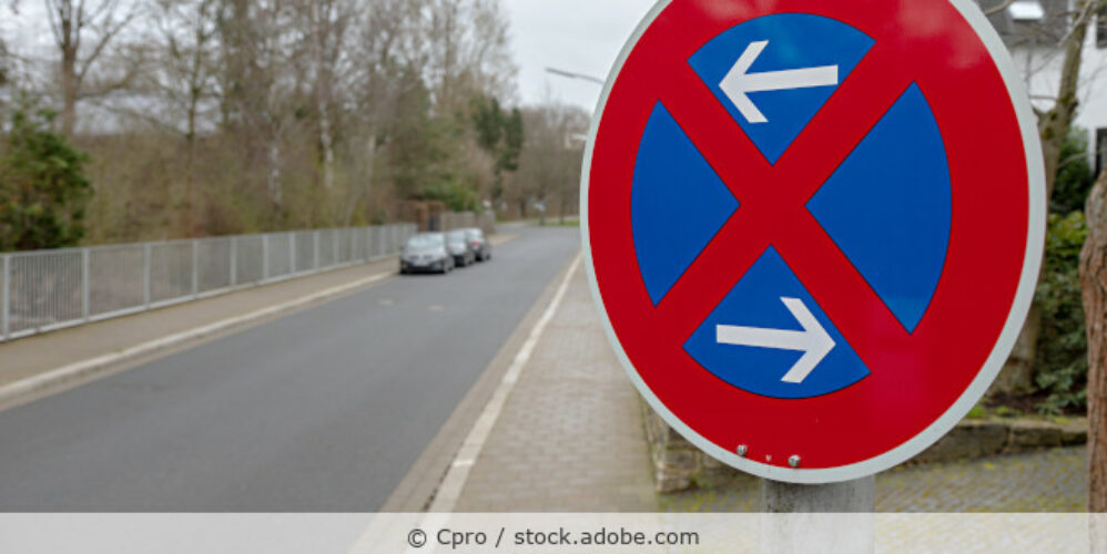 Straße in einem Wohngebiet mit parkenden Autos und einem Halteverbotsschild im Vordergrund.