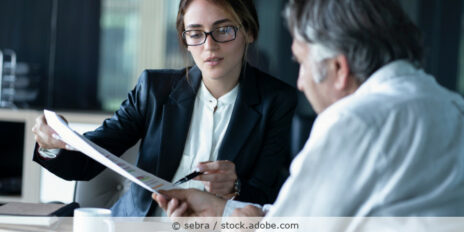 Frau und Mann sitzen im Büro am Tisch und sprechen über ein Dokument.