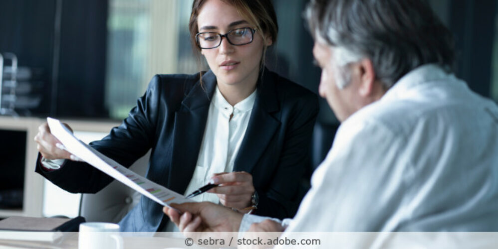 Frau und Mann sitzen im Büro am Tisch und sprechen über ein Dokument.