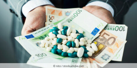 Mann im Anzug hält Geldscheine und Tabletten in seinen geöffneten Händen vor sich.