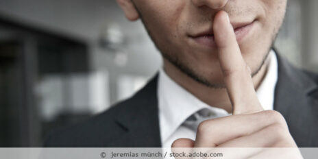 Mann im Anzug legt den Finger auf den Mund als Zeichen zu schweigen.