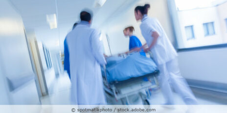 Medizinisches Personal schiebt einen Patienten im Krankenbett einen Flur entlang.