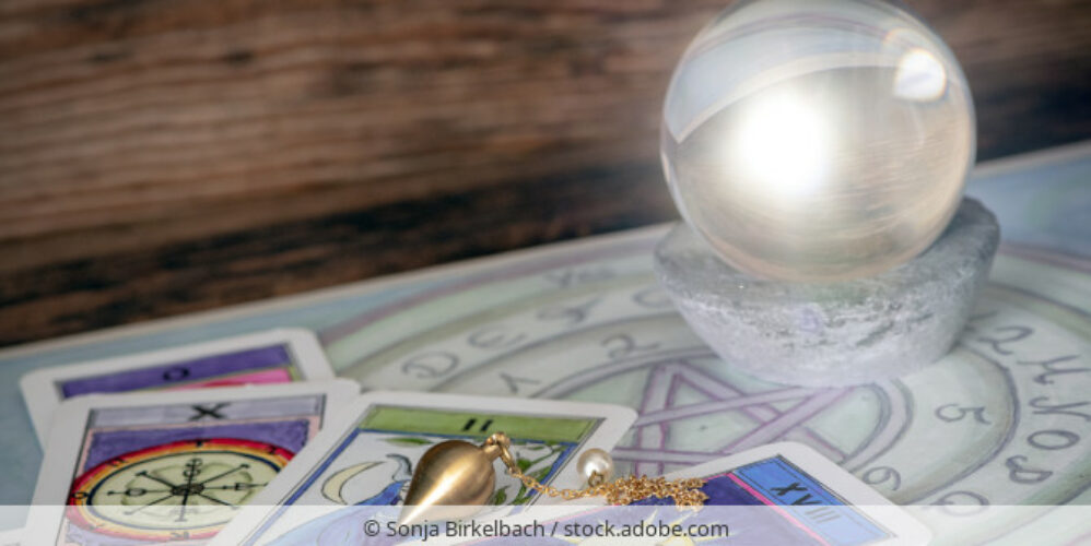 Glaskugel, Tarotkarten und ein Pendel auf einem Ouija-Brett.